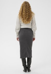 Sivá denim sukňa s rovnou siluetou a rozparkom vzadu, skombinovaná s svetlo sivým štruktúrovaným sveterom a čiernymi čižmami po kolená.