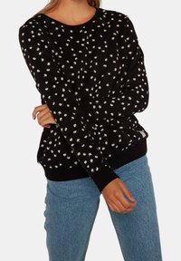 Felpa nera con motivo floreale bianco, colletto e polsini a coste. Caratterizzata da una vestibilità comoda e una consistenza morbida, abbinata a jeans blu.