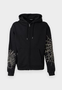 Melna zipa hoodie ar priekšējām kabatām un baltām zirnekl tīkla dizainiem uz abām piedurknēm, ar kapuci, kuru var regulēt ar saitēm.