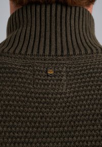 Tamnozeleni pletivni pulover s debelim rebrastim ovratnikom i teksturiranim tijelom. Ima mali, okrugli logotip na leđima.