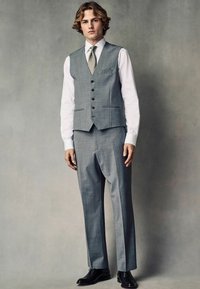 Traje gris de tres piezas con chaleco con muescas, camisa blanca y corbata texturada; presenta botones negros, corte entallado y zapatos negros.