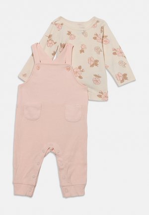 Salopette bébé rose côtelée avec fermetures pression et poches avant, associée à une chemise crème à manches longues décorée d'un imprimé floral rose.