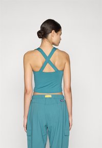 Teal verkürztes Tanktop mit Rückenkreuzträgern, kombiniert mit passenden teal-farbenen Cargo-Hosen, die seitliche Taschen und einen elastischen Bund haben.