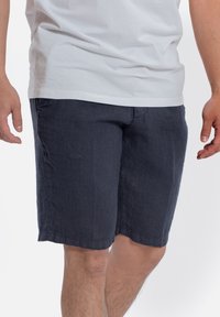 Granatowe lniane szorty o luźnym kroju, z bocznymi kieszeniami i prostym wykończeniem. Tekstura materiału wydaje się lekka i przepuszczająca powietrze.