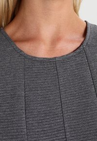 Grå, ribbad tygtröja med rund halsringning och subtila sömnadsdetaljer, som visar en strukturerad yta och en något åtsittande design.