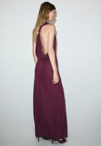 Robe longue bordeaux avec un dos drapé et un col halter. Confectionnée en tissu doux et fluide, elle présente un dos décolleté et une texture lisse.