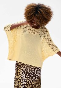 Żółty sweter w otwartym splocie z szerokimi rękawami, w połączeniu z brąską spódnicą z jasnym wzorem na leopardzie.