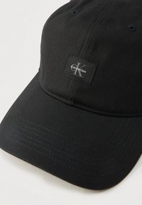 Μαύρο καπέλο baseball Calvin Klein με καμπυλωτό γείσο και ραμμένο λογότυπο στο μπροστινό πάνελ, τοποθετημένο σε λευκή επιφάνεια.