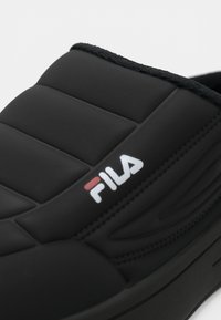 Svart slip-on sko med polstret overdel, teksturerte detaljer og hevet gummisåle. Har en hvit og rød Fila-logo på siden.