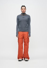 Top cinzento de manga comprida com gola com fecho e detalhe amarelo, combinado com calças cargo laranja largas com bolsos laterais.