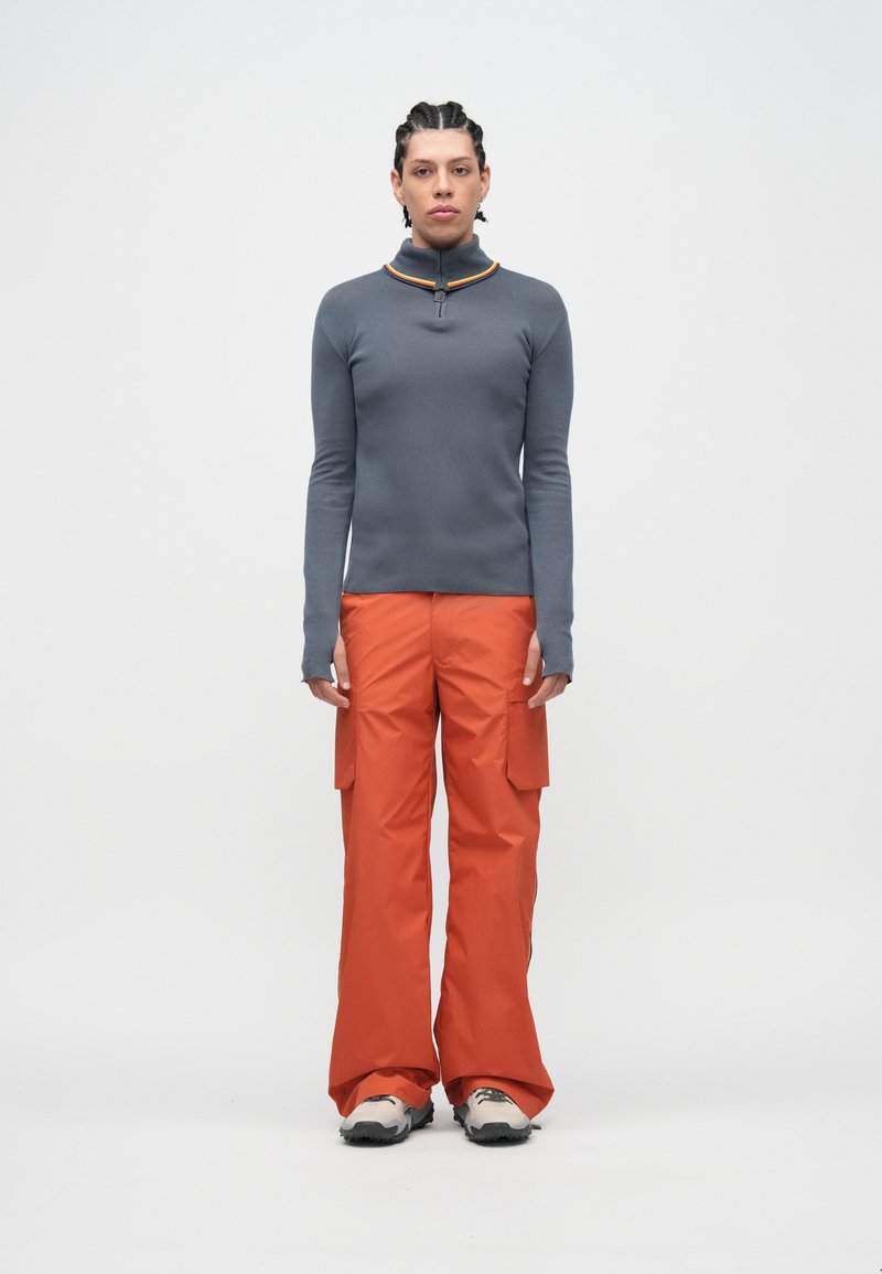 Top cinzento de manga comprida com gola com fecho e detalhe amarelo, combinado com calças cargo laranja largas com bolsos laterais.