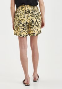 Keltaiset shortsit mustalla kukkakuviolla, elastisella vyötäröllä ja löysällä istuvuudella. Yhdistetty ruskeisiin litteisiin sandaaleihin.