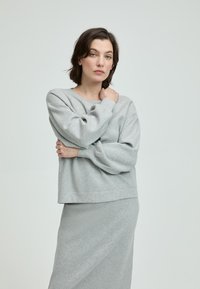 Hellgrauer Strickpullover mit lockerer Passform und weiten Ärmeln, kombiniert mit einem passenden hellgrauen Rock. Weiche Textur und einfaches Design.