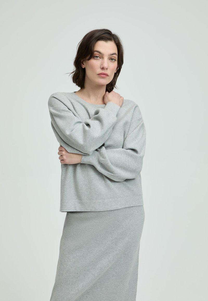 Hellgrauer Strickpullover mit lockerer Passform und weiten Ärmeln, kombiniert mit einem passenden hellgrauen Rock. Weiche Textur und einfaches Design.