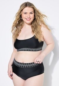 Set di bikini nero composto da un top corto e slip a vita alta, decorato con un motivo a zigzag bianco lungo l'elastico in vita. Texture liscia.