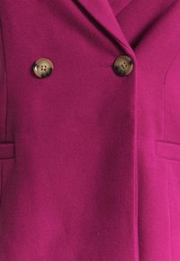 Fuchsia uld blazer med dobbeltradet design, spids krave og to store, runde brune knapper med fire huller hver.