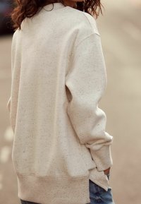 Sudadera color beige claro con una textura moteada, corte relajado, costuras de hombro caídas y puños de canalé. Detalle de dobladillo con abertura lateral.