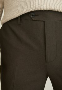 Donkerbruine broek van gestructureerde stof, met een enkele knoopsluiting, voorvouwen en schuine zakken.