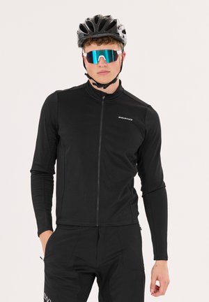 Schwarze Radsportjacke mit langen Ärmeln, Reißverschluss und strukturiertem Stoff. Getragen mit einem schwarzen Helm und blaufärbigen Sonnenbrillen.