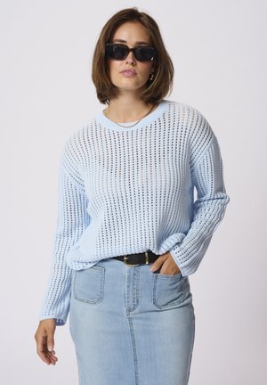 Lyseblå, strikket sweater med løs, åben vævning og lange ærmer. Sammen med en lyseblå denimnederdel og et sort bælte.