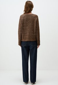 Pull en maille marron avec une finition texturée, un col rond et un design court, associé à un jeans large bleu foncé.