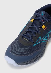 Marineblå løpesko med teksturert overflate, GORE-TEX-merke og livlige akvamarinfargede og gule aksenter i det øverste designet.