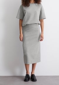 Szara bluzka z bawełnianej mieszanki z oversized rękawami w zestawie z dopasowaną ołówkową spódnicą do połowy łydki. Czarne wsuwane buty dopełniają stylizację.