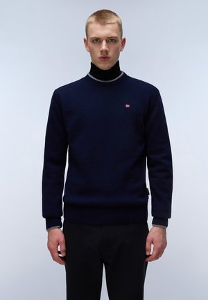 Maglione a maglia blu navy con collo rotondo e orlo a coste. Presenta un piccolo logo rosso e bianco sul petto. Maniche lunghe con polsini a contrasto.