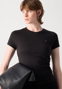 T-shirt en coton noir à manches courtes, col rond et petit logo multicolore sur la poitrine. Tenue avec une grande pochette en cuir noir.