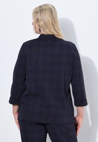 Giacca a quadri blu navy con maniche arrotolate, presenta un tessuto texturizzato e una linea dritta, con accenti arancioni a rete.