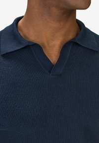 Mörkblå v-ringad stickad tröja med ribbstruktur och platt krage. Tyget verkar mjukt och något stretchigt.