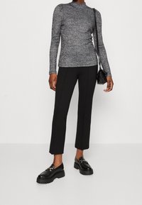 Haut gris à manches longues tacheté avec un col montant, associé à un pantalon noir ajusté et des chaussures noires épaisses ornées d'un accent en chaîne décorative.