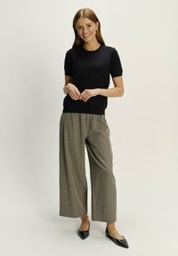 Black short-sleeve top with a round neckline paired with wide-leg plaid trousers in earthy tones and black pointed-toe shoes.
