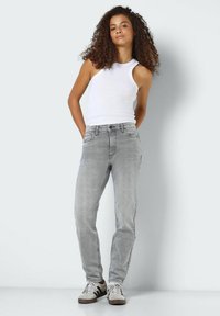Light grey jeans with a straight-leg fit, medium wash, and five-pocket design, paired with a white tank top and casual sneakers.