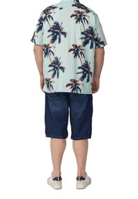 Korte mouwen, lichtblauwe shirt met een donker palmboompatroon, gecombineerd met een donkere spijkerbroekshort en witte sneakers met rode en marineblauwe accenten.