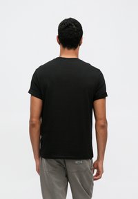 Fekete pamut póló rövid ujjakkal és felhajtott mandzsettákkal, kerek nyakkivágással és egyszerű, egyszínű mintával. Nincsenek látható logók vagy minták.