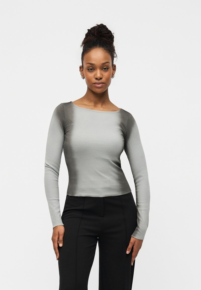 Μπλούζα μακρυμάνικη σε ανοιχτό γκρι με απαλή υφή, με φαρδύ ντεκολτέ και εφαρμοστή σχεδίαση, συνδυασμένη με μαύρο παντελόνι.