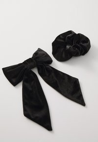 Black velvet hair accessories: a large bow with long tails and a matching scrunchie. Both feature a soft, smooth texture.