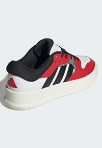 Sneaker rosso e bianco con dettagli neri, dotato di una parte superiore testurizzata, una suola bianca spessa e tre strisce nere sul lato.