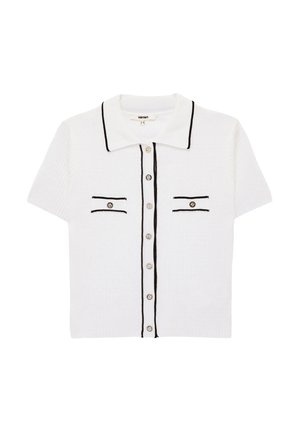 Valkoinen lyhythihainen neulecardigan mustalla reunuksella, edessä napit, terävä kaulus ja kaksi napillista rintataskua.