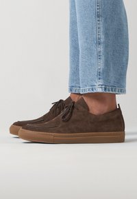 Chaussures en daim marron avec un profil bas et un bout arrondi, présentant un design à lacets, une semelle en caoutchouc et des détails de couture subtils.
