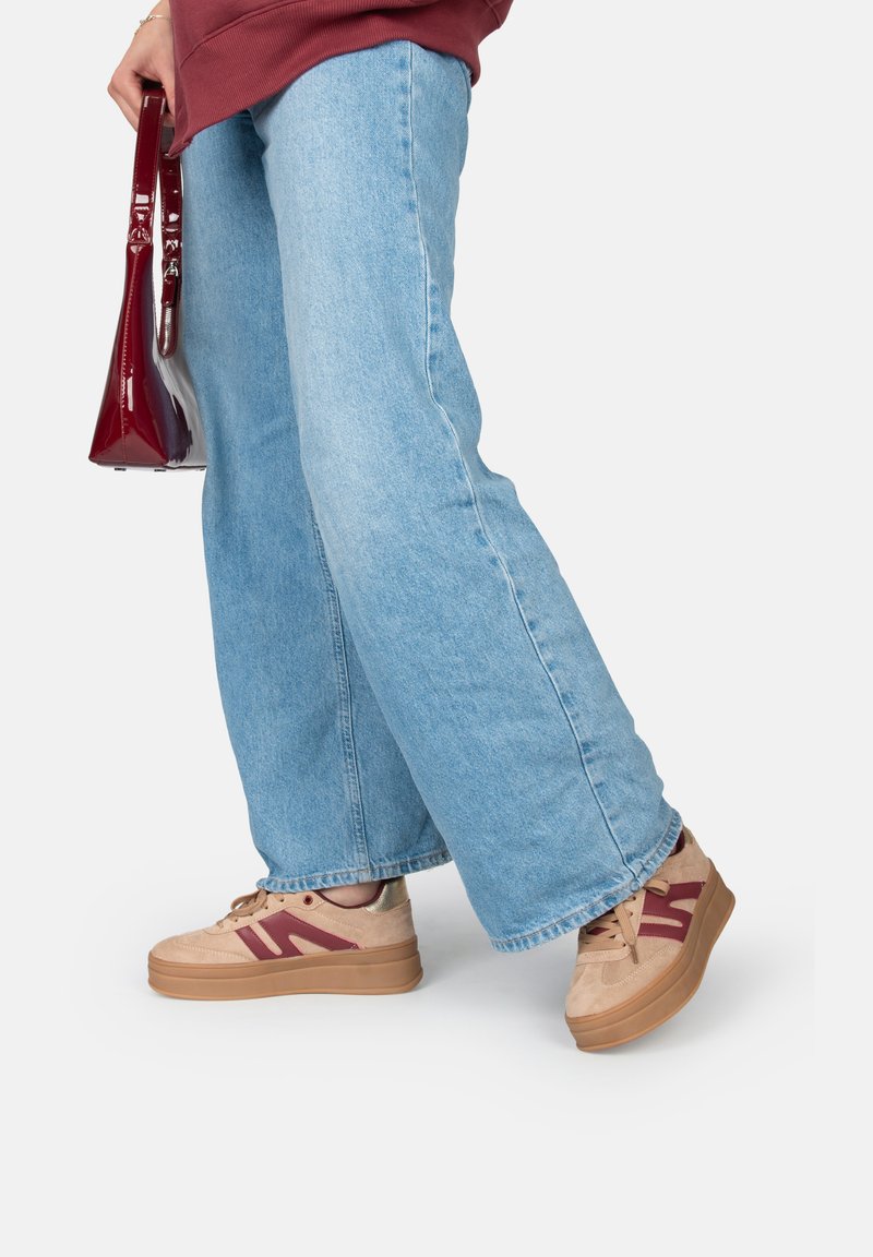 Sneakers platform beige con accenti bordeaux, materiale scamosciato e suola in gomma testurizzata. Abbinati a jeans larghi blu chiaro e una borsa bordeaux.