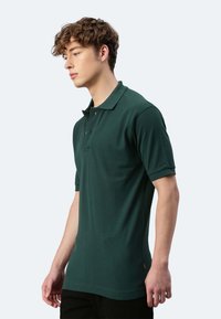 Polo shirt verde scuro realizzato in tessuto morbido, con colletto classico, maniche corte e vestibilità slim, con un sottile dettaglio del logo sull'orlo.