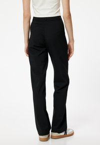 Zwarte op maat gemaakte pantalons met een recht gesneden pijp, voorzien van een gladde textuur en subtiele zijzakken. Draag ze met witte sneakers.