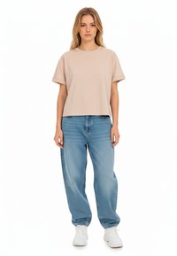 T-shirt in cotone beige chiaro, maniche corte, vestibilità rilassata, abbinato a jeans a vita alta blu chiaro, sneakers bianche, design minimal.