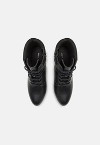 Botas negras de cuero liso para tobillo con cordones en la parte frontal, punta redondeada y cierre con cremallera en los laterales. Forro interior suave visible.