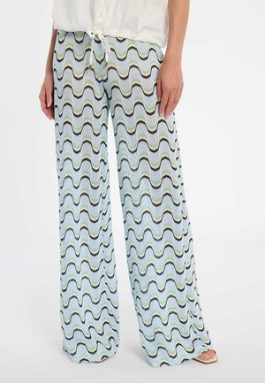 Hose mit weitem Bein und wellenförmigen Streifen in Blau, Grün und Schwarz, getragen mit einem weißen Top mit Kordelzug und beigen offenen Schuhen.