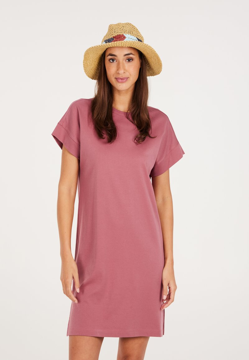 Rosa T-Shirt-Kleid mit kurzen Ärmeln, aus weichem Stoff. Das Modell trägt einen natürlichen Strohhut mit blauen und roten Akzentbändern.