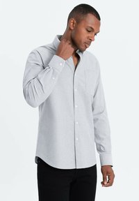 Vaaleanharmaa nappipaita, jossa on rintatasku, pitkät hihat ja kaulus, valmistettu teksturoidusta kankaasta. Yhdistetty mustiin housuihin.