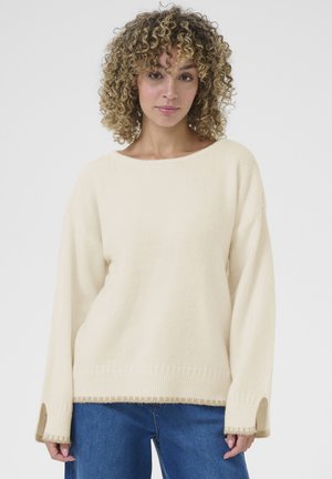 Cream-colored knitted sweater with a wide neckline, long sleeves, side slits, and ribbed hem. Soft texture and relaxed fit.